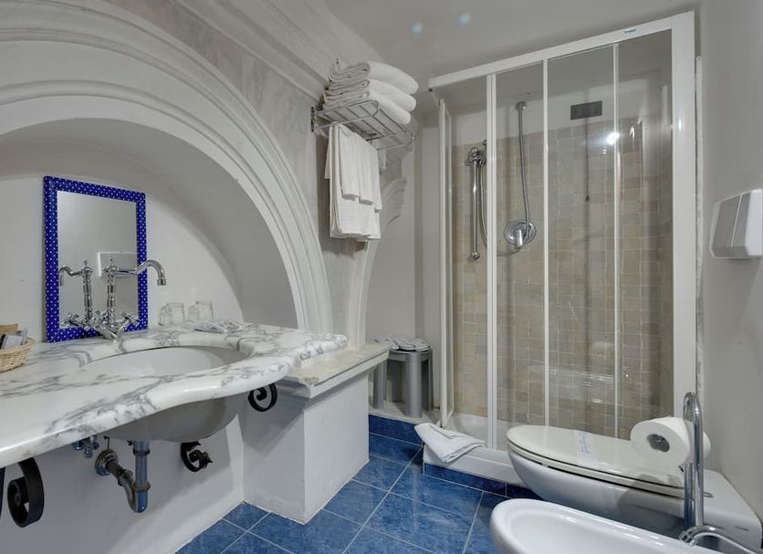 Hotel De La Ville bathroom in Civitavecchia with marble vanity, blue tile floor, and glass shower