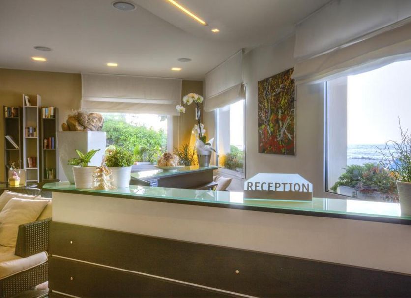 Hotel La Baia reception desk with potted plants and sea view through windows in Diano Marina