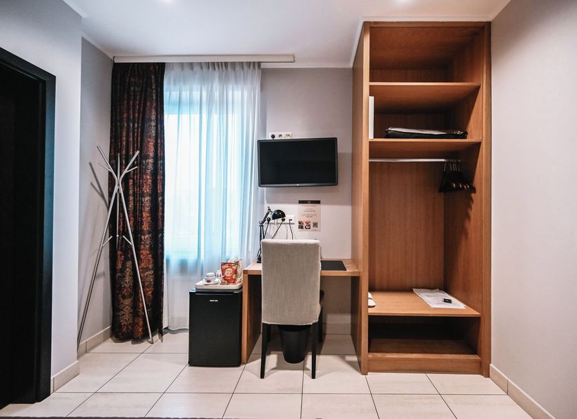 Hotel Pax Luxembourg guest room with desk, chair, wall-mounted TV, wardrobe, and window with curtains