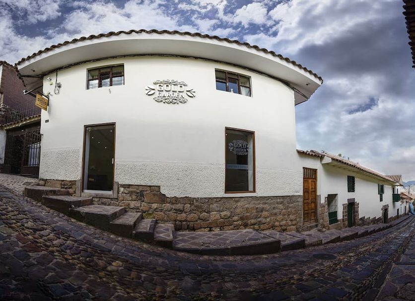 Hotel Boutique Gold Garden in Cusco, white curved corner building on a cobblestone street under cloudy sky