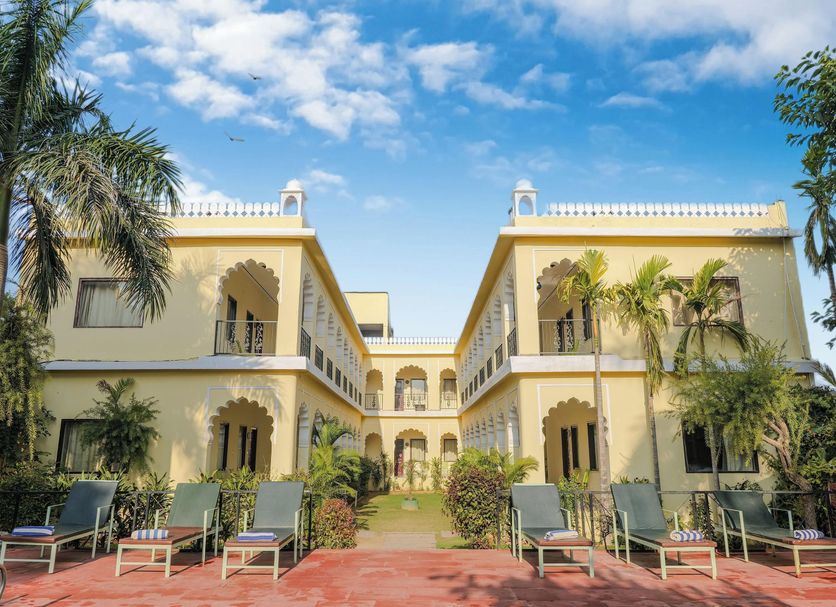 Raj Palace Resort in Sawāi Madhopur with a courtyard and palm trees under a blue sky