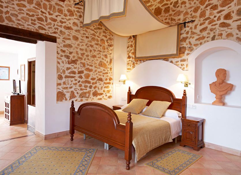 Agroturismo Puig de Ros d'Alt in S'Arenal bedroom with stone walls, wood bed, and arched alcove bust.