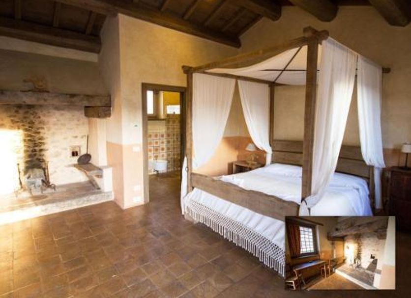 Agriturismo Il Casale Degli Amici in Norcia: rustic bedroom with four-poster bed and stone fireplace