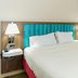 Hampton Inn Garden City bed with white linens, turquoise headboard and bedside lamps in guest room