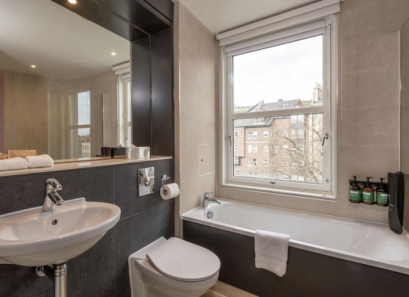 Apex City of Edinburgh Hotel bathroom with bathtub, sink and window view over Edinburgh
