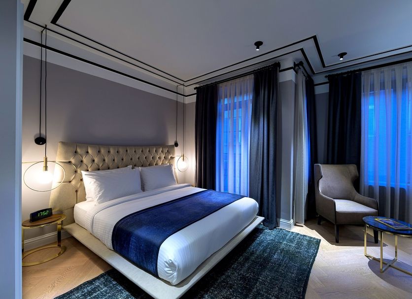 Walton Hotels Galata Istanbul guest room with king bed, blue throw, curtains and accent chair
