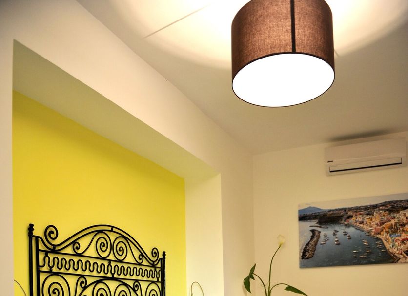 Il Leone di Mare, Procida: bright guest room with wrought-iron bed, yellow accent wall, and patterned floor