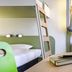 Ibis Budget Dresden Kesselsdorf guest room with bed, desk, luggage rack, and hanging jacket in Kesselsdorf