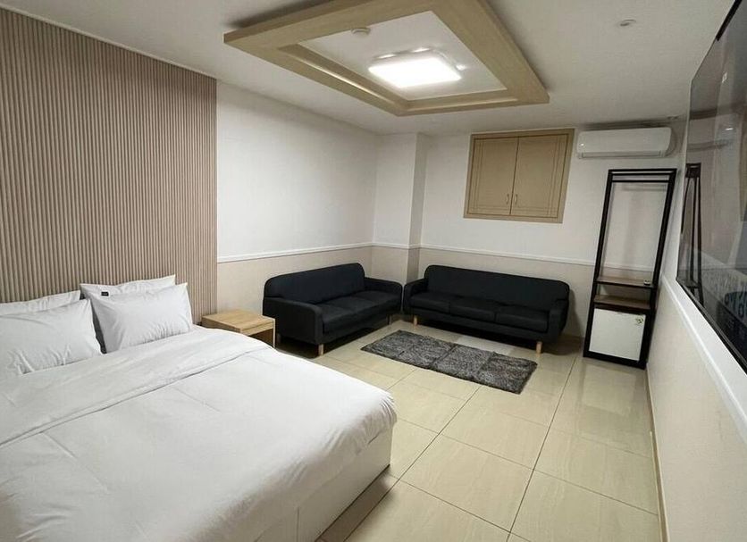 Jm Hotel in Suwon guest room with bed, two black sofas, rug and wall-mounted TV