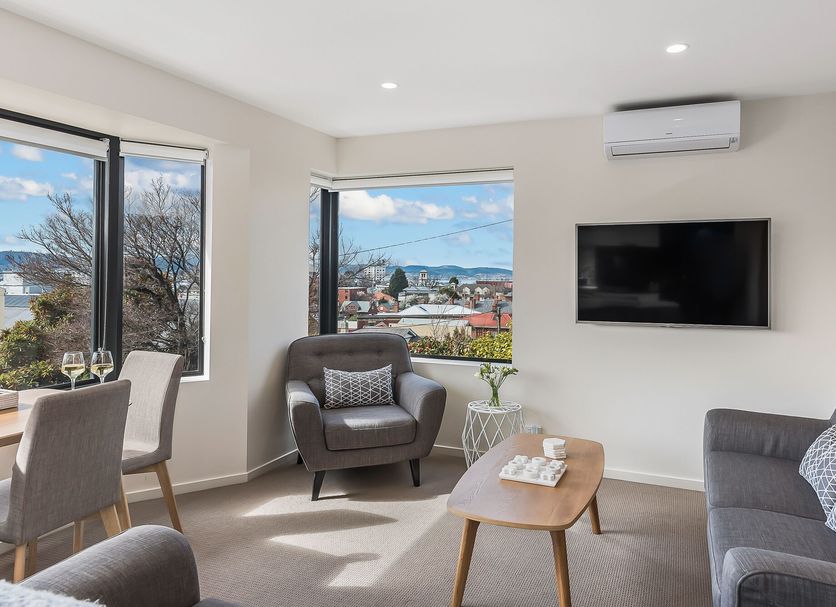 110 Hampden Apartments Hobart living room with city and water views, wall-mounted TV and armchairs