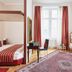 Living Hotel an der Oper Vienna guest room with canopy bed, desk, window, and patterned rug