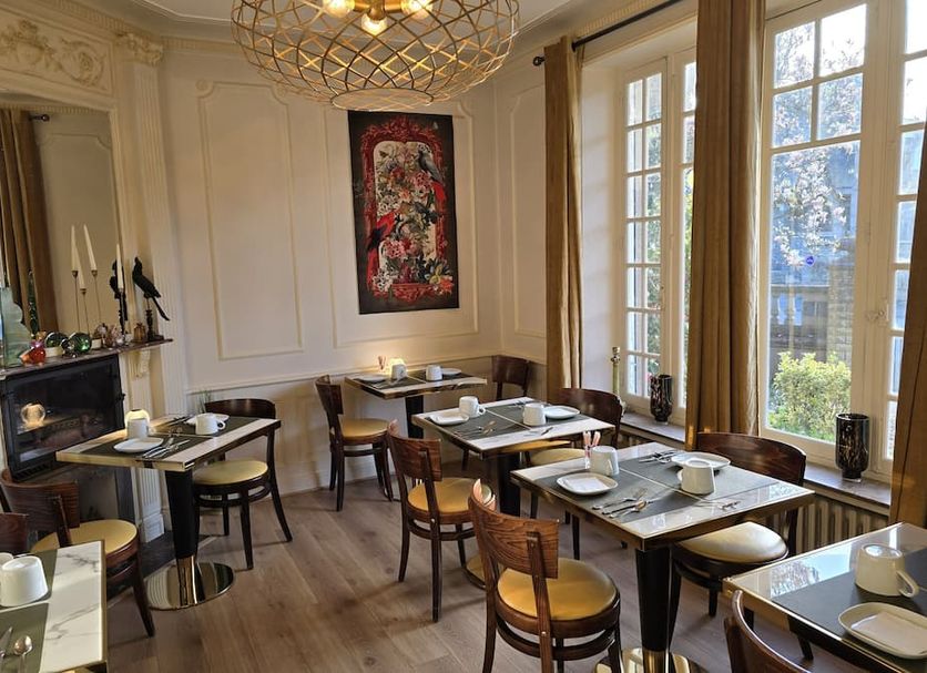 Le Castel Guesthouse in Bayeux dining room with set tables, fireplace, and large windows