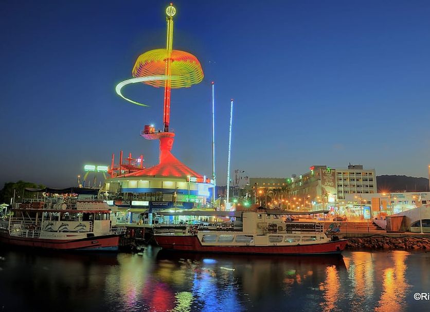 Brown Eilat waterfront view with illuminated marina, boats, and city lights at dusk in Eilat