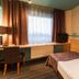Ibis Styles Riga guest room with bed, desk, chair and city view through curtained window
