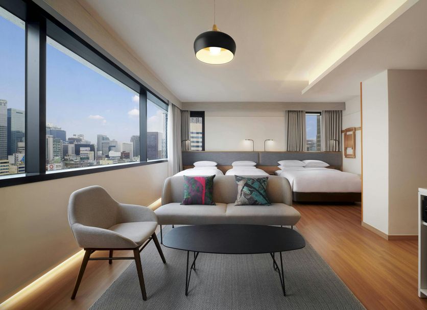 Moxy Seoul Insadong room with city-view windows, three beds, and a lounge chair in Seoul