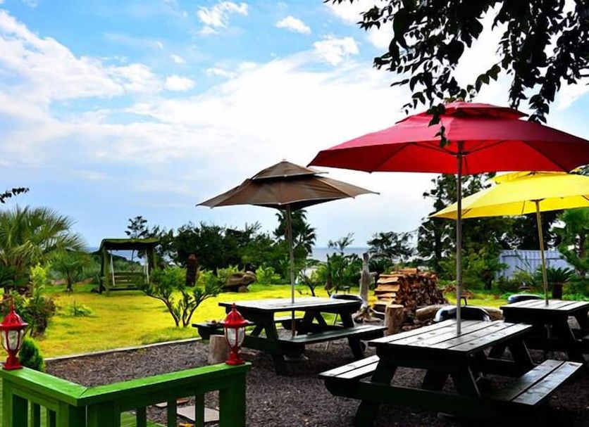 Jeju Bada Wi Olle Pension in Seogwipo, outdoor garden with picnic tables, umbrellas, and sea view