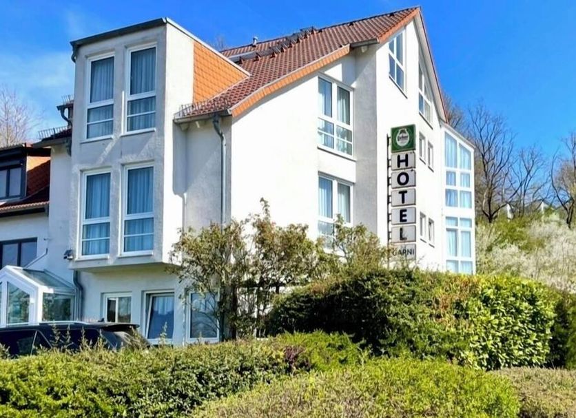 Hotel Garni Niedernhausen in Niedernhausen, white 3-story hotel with sloped roof and greenery