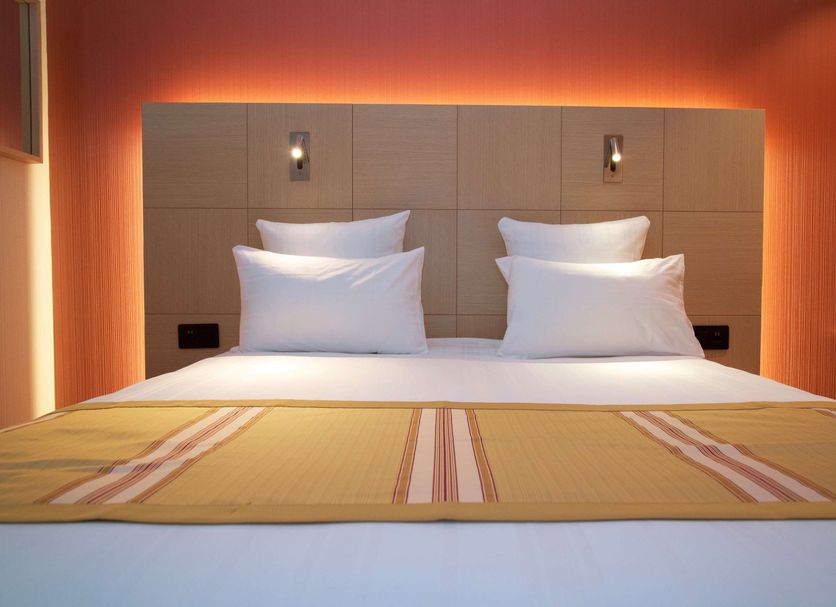 Nash Airport Hotel in Meyrin guest room with double bed, warm orange lighting and wall-mounted lamps