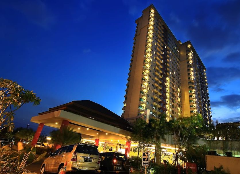 Solo Paragon Hotel & Residences in Surakarta City, tall lit tower at dusk with driveway and parked cars