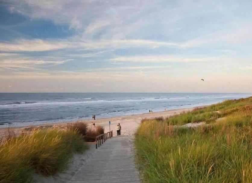 Strandhotel Achtert Diek in Langeoog with boardwalk to sandy beach and ocean under a pastel sky