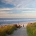 Strandhotel Achtert Diek in Langeoog with boardwalk to sandy beach and ocean under a pastel sky