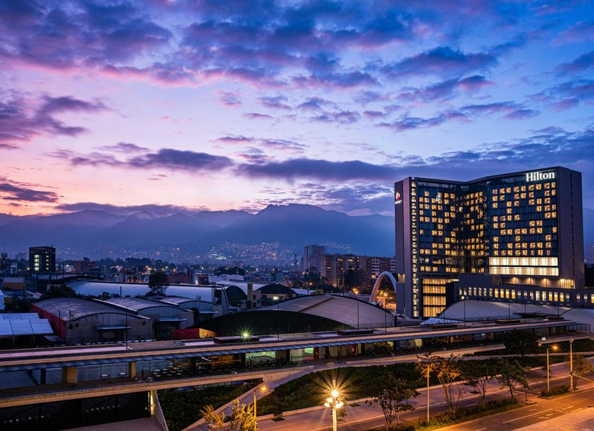 Hilton Bogota Corferias in Bogotá at dusk, with lit windows and city skyline under a colorful sky
