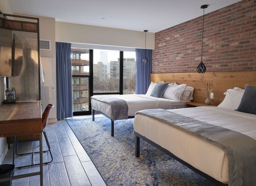 The Maj Hotel in Philadelphia guest room with two beds, brick accent wall, desk, and city view