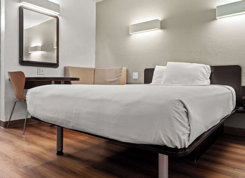 Studio 6 San Luis Obispo Ca South room with queen bed, desk, chair, wall mirror, and wood flooring
