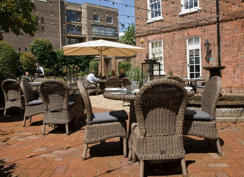 Outdoor courtyard seating at Hotel du Vin Winchester, with wicker chairs, umbrella, and brick buildings in Winchester