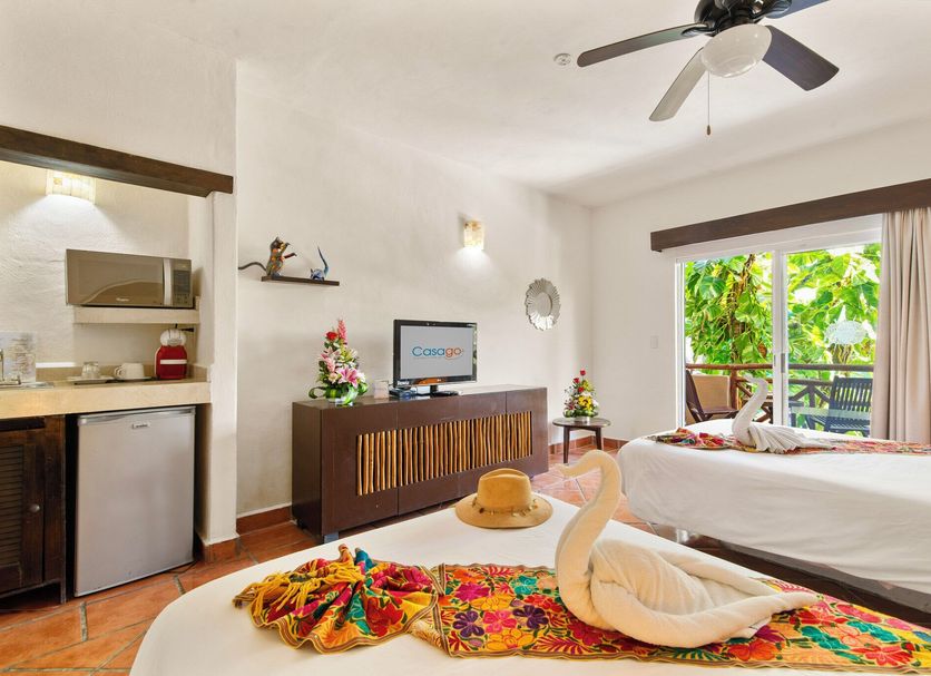 Riviera del Sol in Playa del Carmen guest room with swan towel art, colorful rug, and balcony garden view
