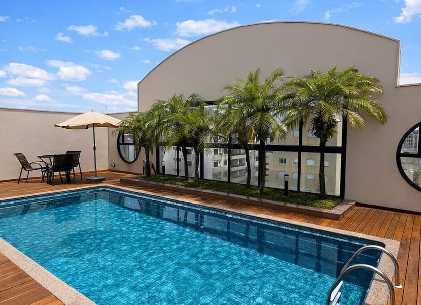 Tsue The Palace Flat in Sao Paulo rooftop pool with palm trees, lounge chairs and city views