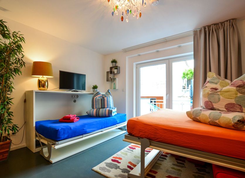 K314 Bonn Aparthotel - Boardinghouse room with sofa bed, bright window, and colorful seating in Bonn