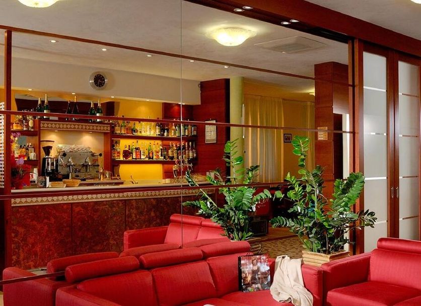 Hotel Odeon, Cervia: red lounge seating facing a hotel bar with mirrored shelving and plants