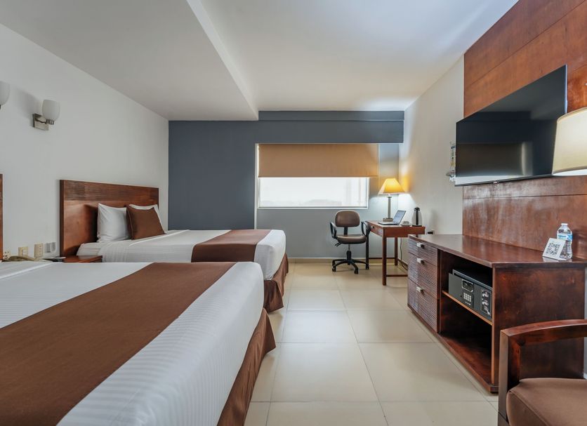 La Venta Inn Villahermosa guest room with two beds, desk, TV and city-view window