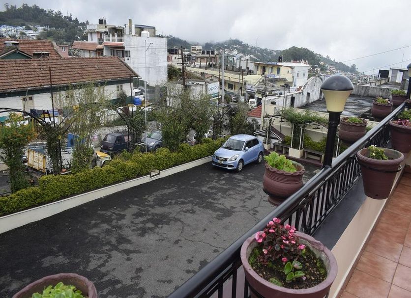 Hotel Apple Valley in Kodaikanal with balcony view of hillside buildings, parked cars and potted flowers
