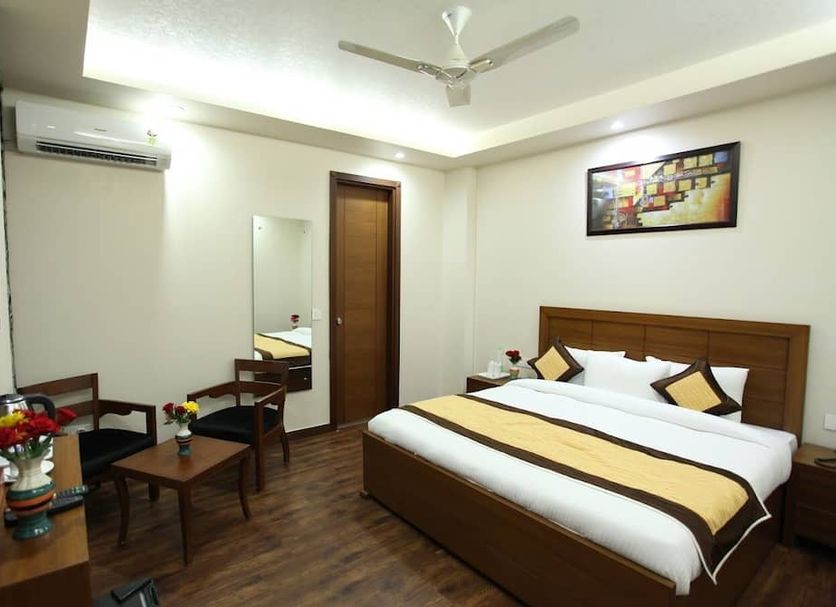 Hotel HC Grand New Delhi room with king bed, seating area, wall mirror and ceiling fan