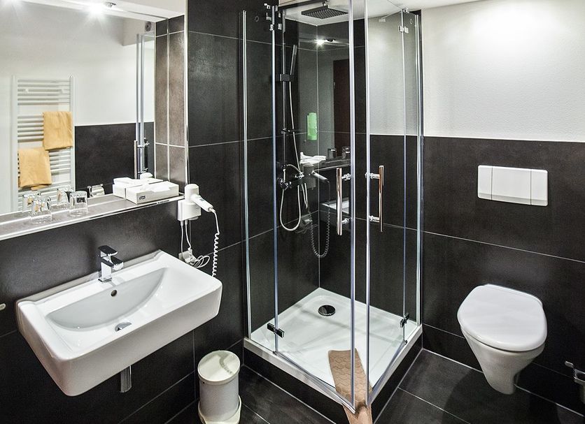 SL'otel Budget Bernburg bathroom with glass shower, wall-mounted sink, toilet and black tile walls