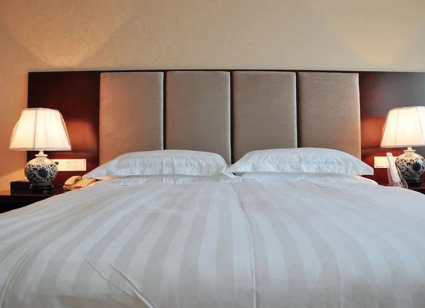 Qilu International Hotel Harbin guest room with king bed, upholstered headboard, and bedside lamps