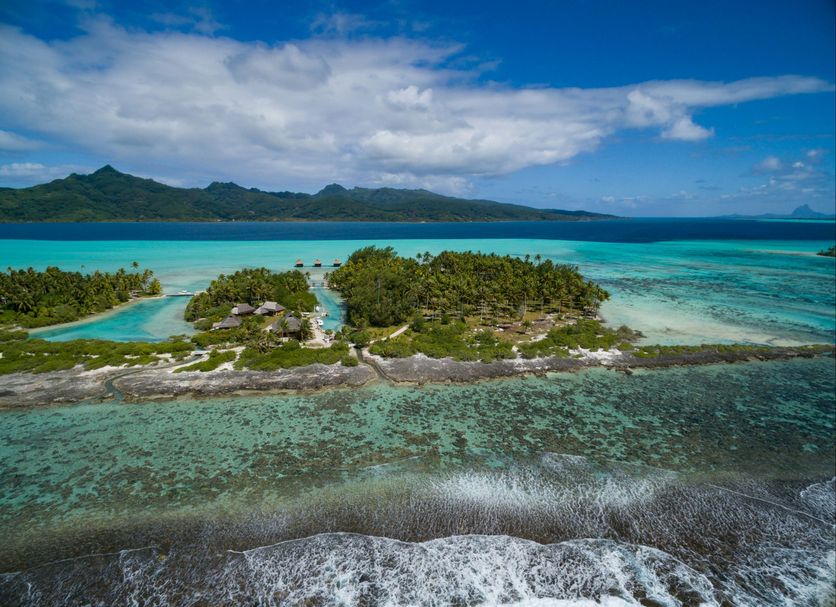 Vahine Private Island in Raiatea with turquoise lagoon, small palm-covered islet, and mountain backdrop