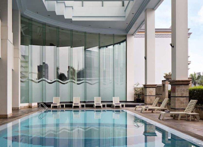 Golden Boutique Hotel Kemayoran in Jakarta with an indoor pool and lounge chairs beside glass walls