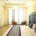 Hotel The Great Ananda in Haridwar: bright guest room with king bed, chairs by window, and patterned curtains