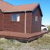 Hagi 1 Guesthouse in Husavik, brown wooden cabin with wraparound deck under blue sky