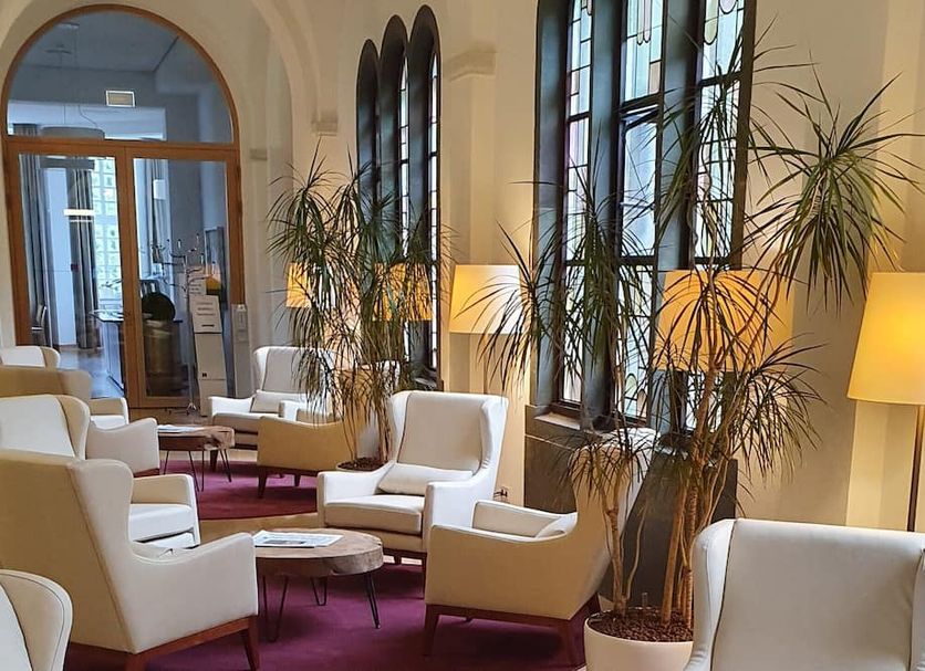 Kardinal Schulte Haus lounge in Bergisch Gladbach with white chairs, tall windows and potted plants
