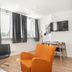 Stay Apartments Einholt Reykjavik room with orange armchair, black chair, wall TV and windows with curtains