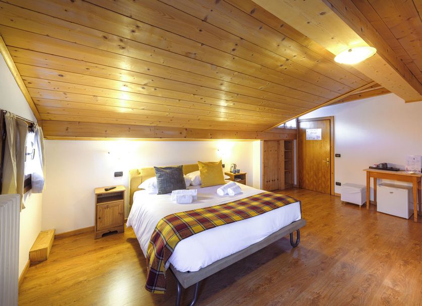Hotel Ambassador Bormio room with double bed, wood-paneled ceiling and hardwood floors in Bormio