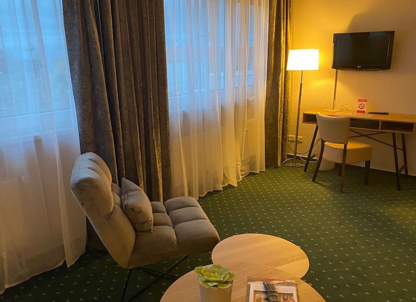 Hotel Westfalia Halle guest room with chair, desk, lamp, wall-mounted TV and large window