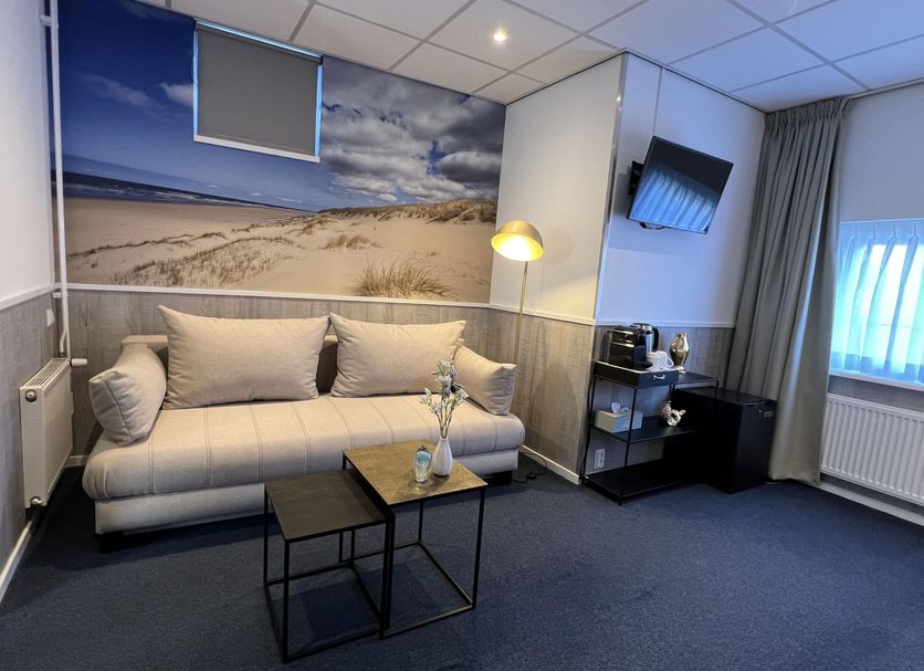 Sea You Hotel Noordwijk room with sofa, wall-mounted TV, beach mural and window curtain in Noordwijk