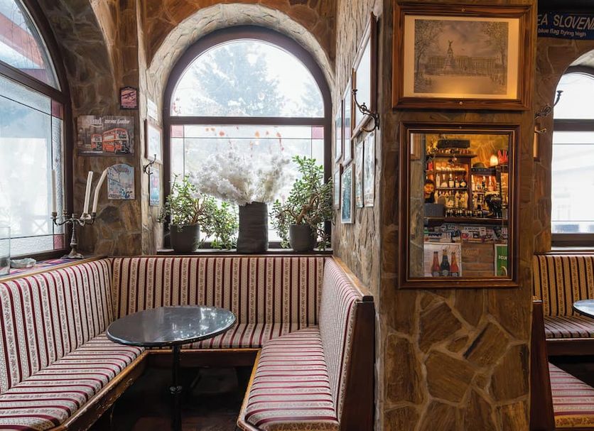 Turn Hostel in Ljubljana: stone-walled lounge with striped benches, arched windows, and small tables