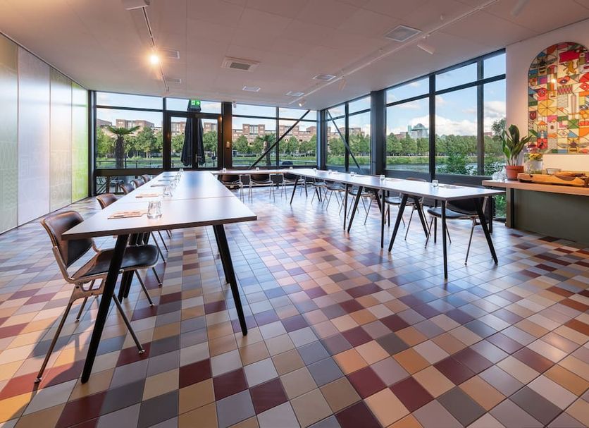Stayokay Maastricht meeting room with tables, colorful tiled floor, and large windows overlooking trees