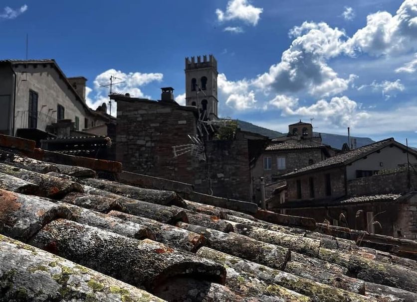 Hotel Lieto Soggiorno in Assisi with rooftop view of stone buildings and a church tower under a blue sky